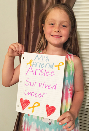 Brooklyn Hutchins holds sign celebrating a friend's successful cancer treatment
