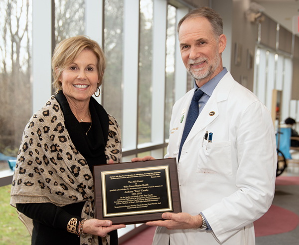 A woman in a leopard shawl smiles at the camera as she receives a plaque from a man in a white coat