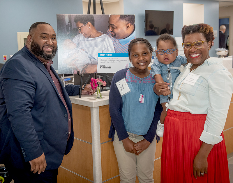 African-American father, mother, daughter and baby son stand in front of a desk in the new Karen and Dale Sisel Neonatal Intensive Care Unit