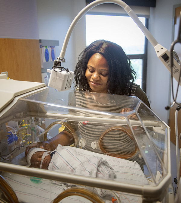 An African-American mother looks down at her baby in a NICU isolette